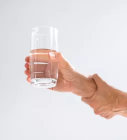 A person holding a glass of water and steading their arm.