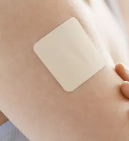 A nondescript, square medication patch is on a person's arm.