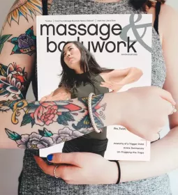 A woman with tattoos on her arms holding a copy of Massage &amp; Bodywork July/August 2023.