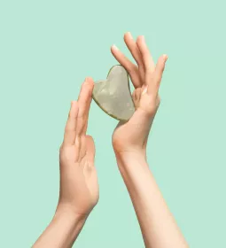 A pair of hands hold a heart-shaped rock.