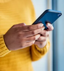 A person in a yellow sweater holding their smartphone with both hands.
