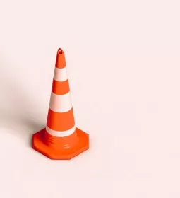 A traffic cone stands by itself on a pink floor.