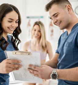 two healthcare providers, one man and one woman, discuss some information and smile.