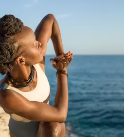 A woman twists and stretches on a cliff near the sea.