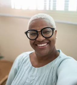 A seated woman with glasses smiling at the camera.