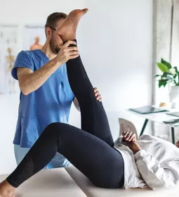 A massage therapist moves a client's leg upward.