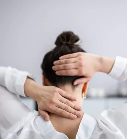A woman feels the base of her neck and touches the back of her head.
