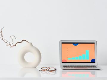 A vase, pair of glasses, and laptop rest on a table.