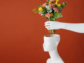 a bouquet of red and yellow flowers is placed into a vase shaped like a head.