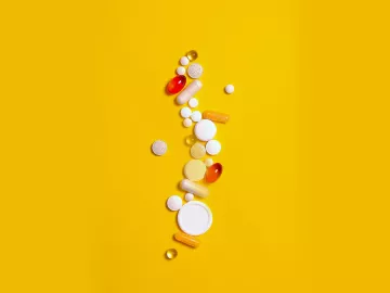 different-shaped pills, tablets, and capsules all scattered across a yellow background.