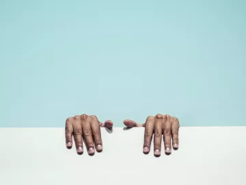 two hands grip a white ledge behind a blue background. 