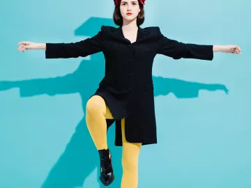 a woman in black and yellow clothes balances a book on her head while standing on one foot.