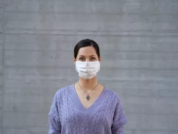 a woman in a purple sweater wears a disposable face mask.