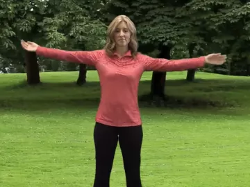 author Angie Parris stands outside on the grass, stretching with her legs and arms outstretched.
