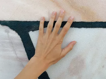 a hand with the palm splayed up against a painted abstract wall.