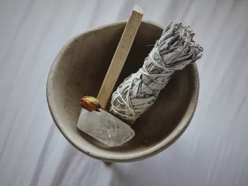 a smudge stick, wood, and a quartz crystal in a bowl.