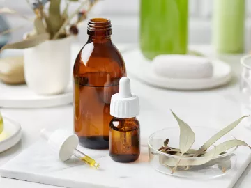 a bottle of essential oil, a dropper, a cup, and a bundle of sage on a table.