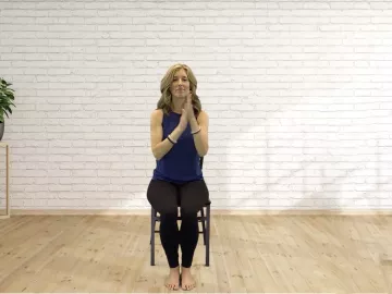Author Angie Parris holds her hands at heart center while sitting in a chair. 