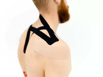 Kinesiology tape applied to a person's back and shoulder.