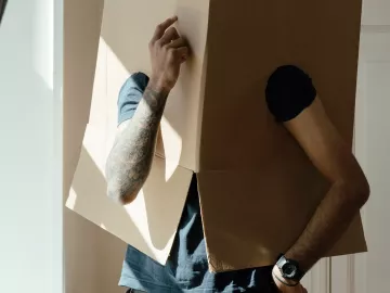 A person wearing a moving box over their head ponders change.