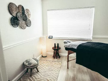 an empty massage room with a wooden table and decor on the wall. the window is open. 