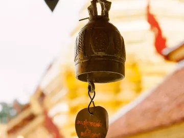 a metal bell hangs outside a gold and yellow wat temple in Thailand.