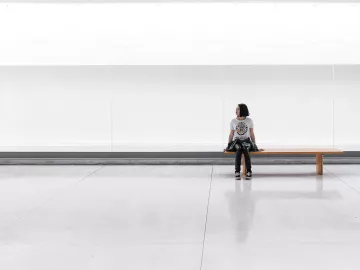 a woman sits on a long bench in an empty room.