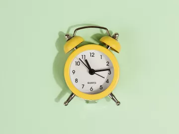 an analog alarm clock against a pale mint-green background.