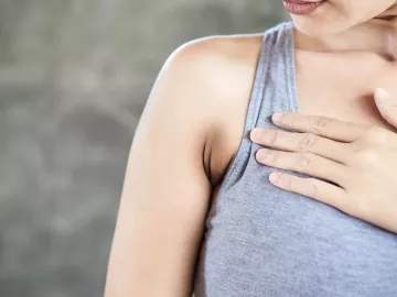 a white woman in a tank top holds a spot on her chest.