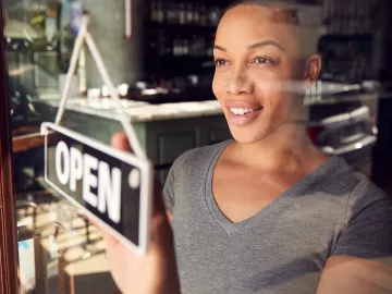 Black woman with short hair changes a business open sign in the window.