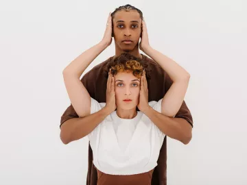 a taller Black person and a shorter White person cover the other's ears with two hands.