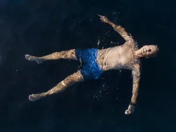 a person in blue swim shorts floats in a dark pool on their back.