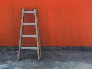 A wooden ladder leans against a red wall.