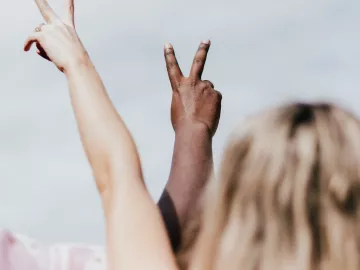 One person with white skin tone and another with dark skin tone make peace signs with their hands.