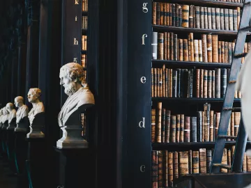 A large, dark library with rows of books and busts of historical figures.