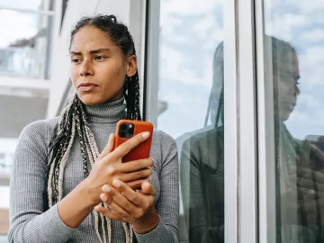A woman holding a smartphone, looking disappointed at a message.