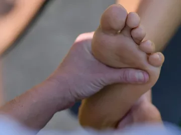 A massage therapist works on the bottom of the left foot of a client.