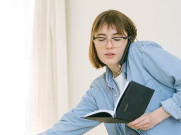 young woman talking on the phone and opening a notebook at the same time.