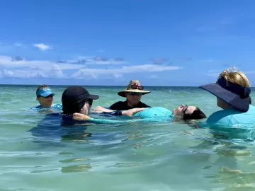 Group of massage therapists support a female client floating in the ocean.
