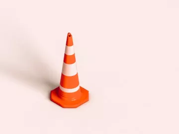 A traffic cone stands by itself on a pink floor.