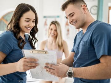 two healthcare providers, one man and one woman, discuss some information and smile.