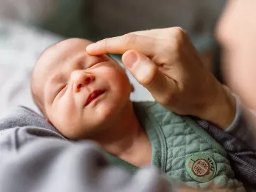 A practitioner delivers craniosacral therapy to a baby but touching the baby above its eyebrow.
