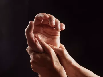 Two hands massage a third hand.