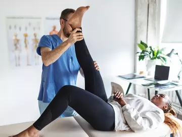 A massage therapist moves a client's leg upward.