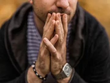 A man holds his hands together in front of his face.