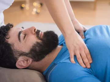 A massage therapist works on a client's pectorals. 