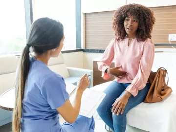 A Black female client points to her stomach in discussion with a therapist.