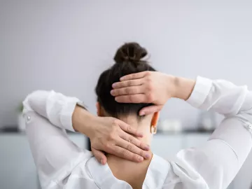 A woman feels the base of her neck and touches the back of her head.
