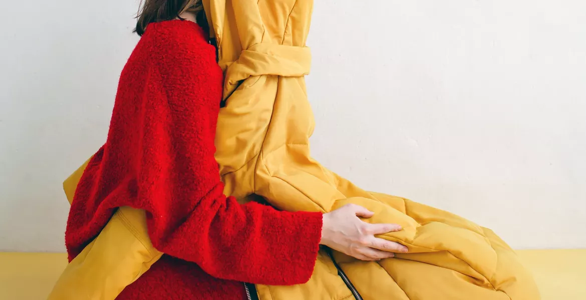 A woman kneels with a jacket covering her face.
