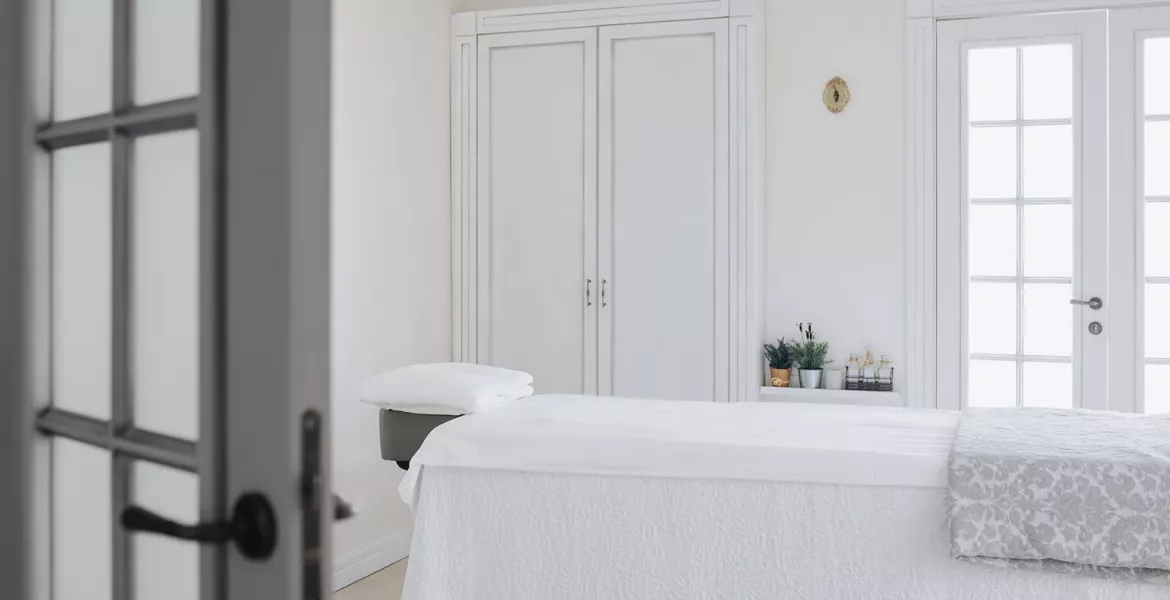 an empty massage table with white sheets and drapes.